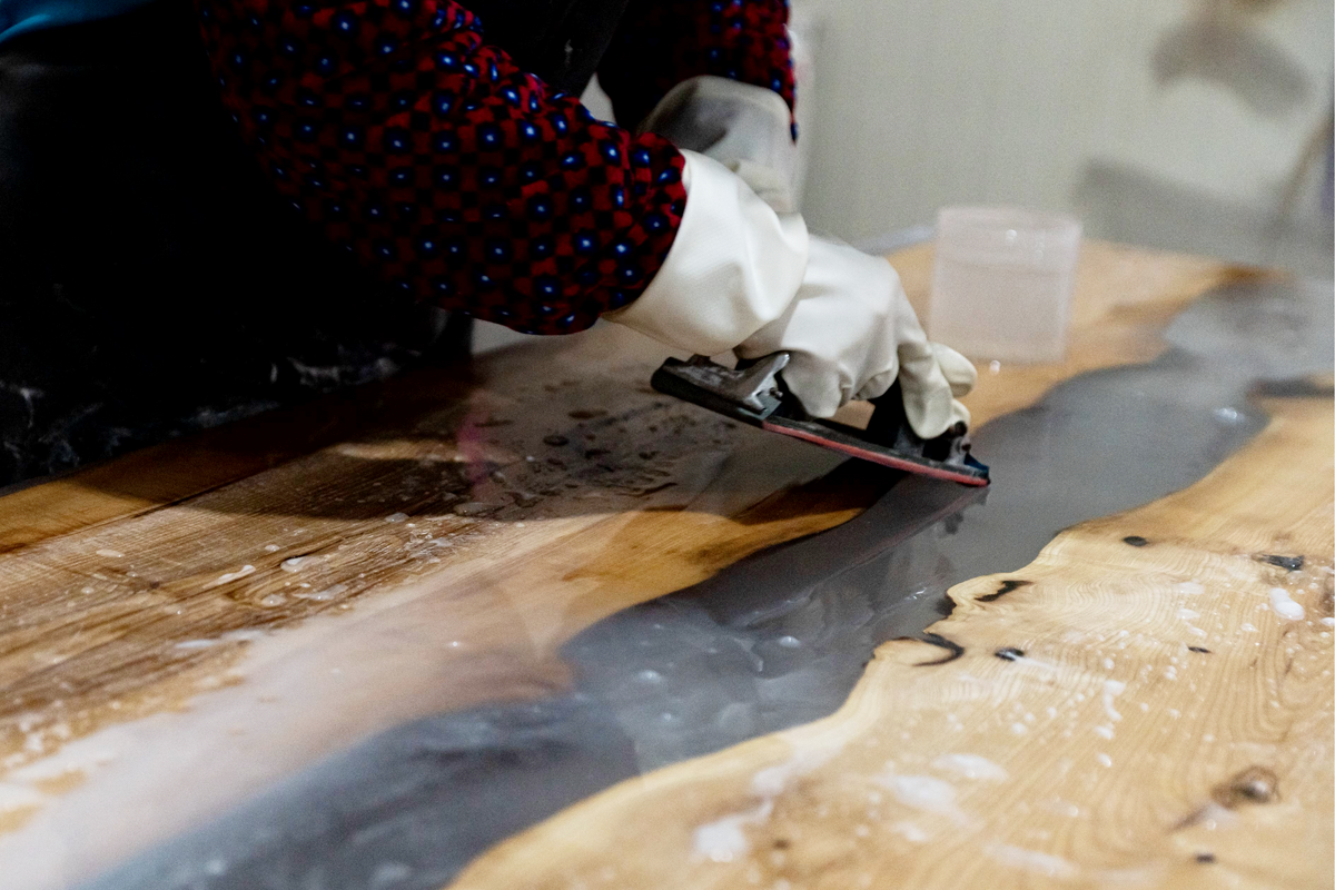 Woodslabs artisan hand-sanding a live-edge walnut table, smoothing the wood surface to reveal its natural grain and character.