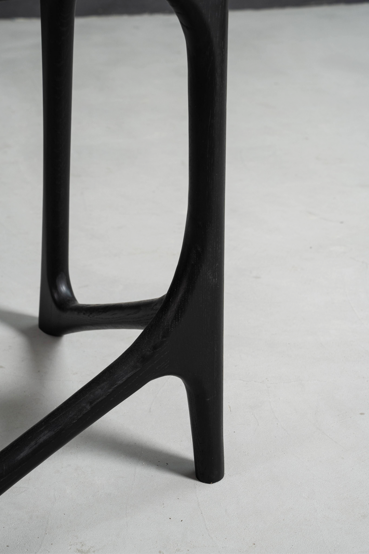 Detailed shot of the Butterfly Effect T-Base's lower section, showing the black stained oak joinery and structural form.