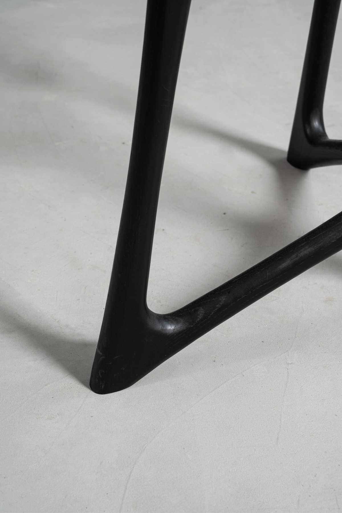 Detailed shot of a Woodslabs black oak Butterfly T-Base meeting the ground, showing the joint and sculptural foot.