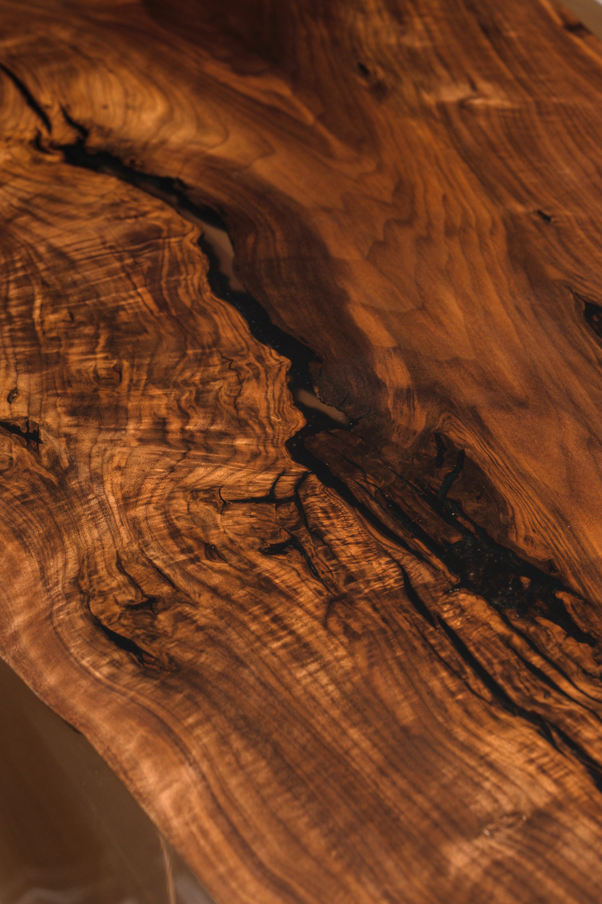 Close-up of the Continental Table's live-edge black walnut shore meeting earth-tone epoxy resin tides.
