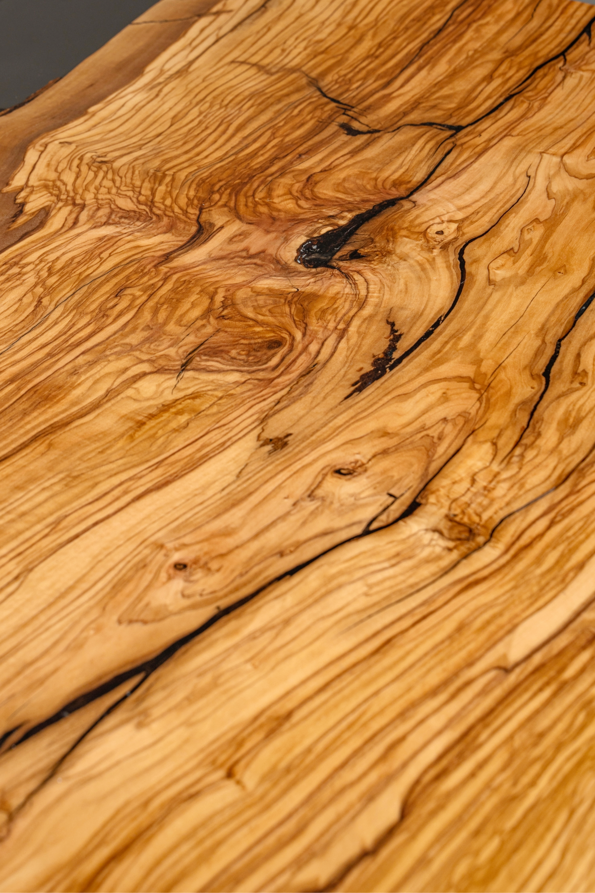 Close-up of the Minerva Table's Italian olive wood surface, showcasing a dramatic burl and swirling grain pattern.