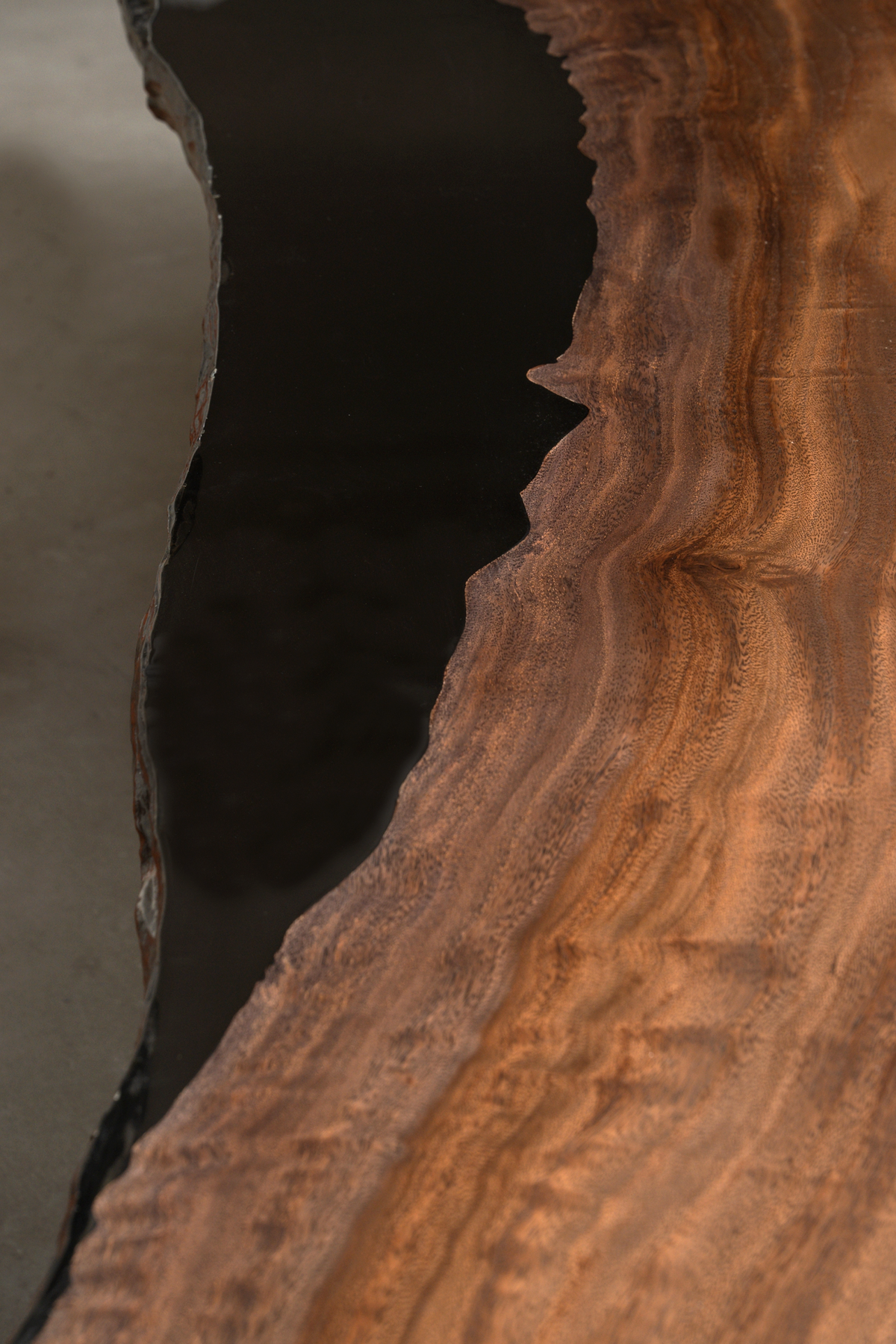 Close-up where the Silent Basin Table's rainwood grain meets the black ice epoxy river, highlighting the seamless fusion.