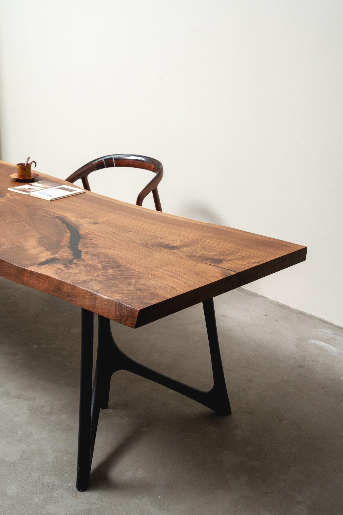 Corner side view of the Span of Influence Table's black walnut butterfly base supporting the live edge wood slab.
