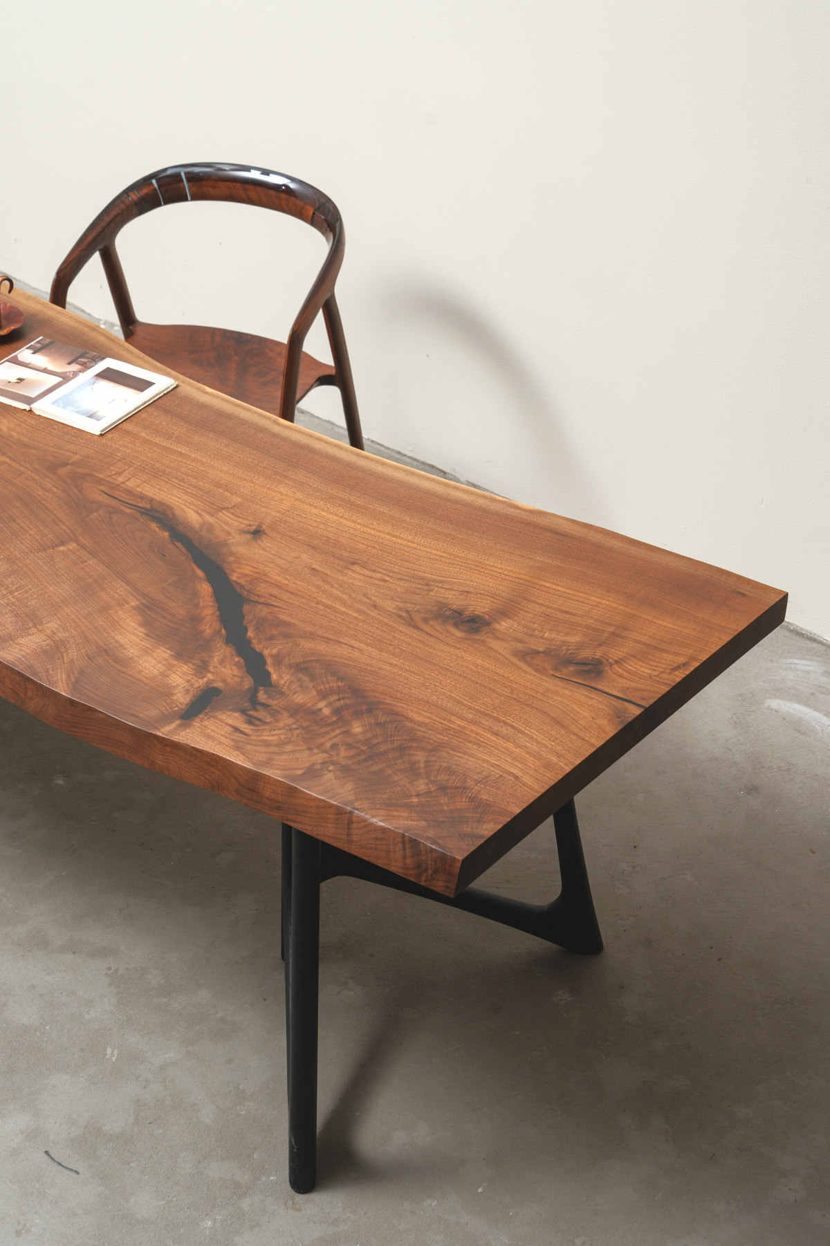 Angled view showcasing the dramatic grain pattern and substantial edge of the Span of Influence black walnut table.
