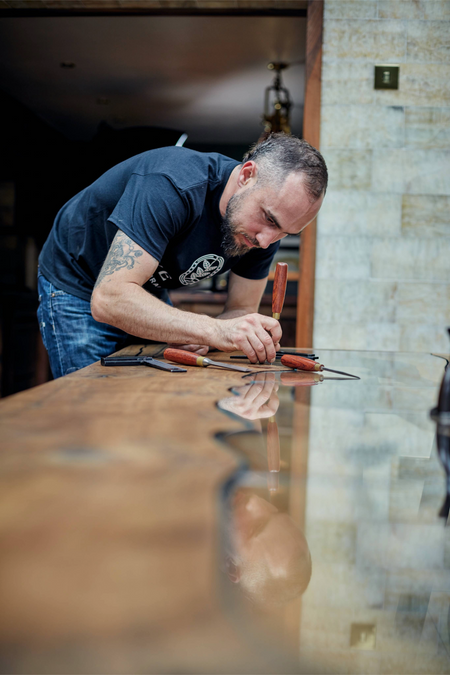 Woodslabs artisan hand-chiseling a live edge dining table with traditional woodworking tools. Premium custom furniture craftsmanship.